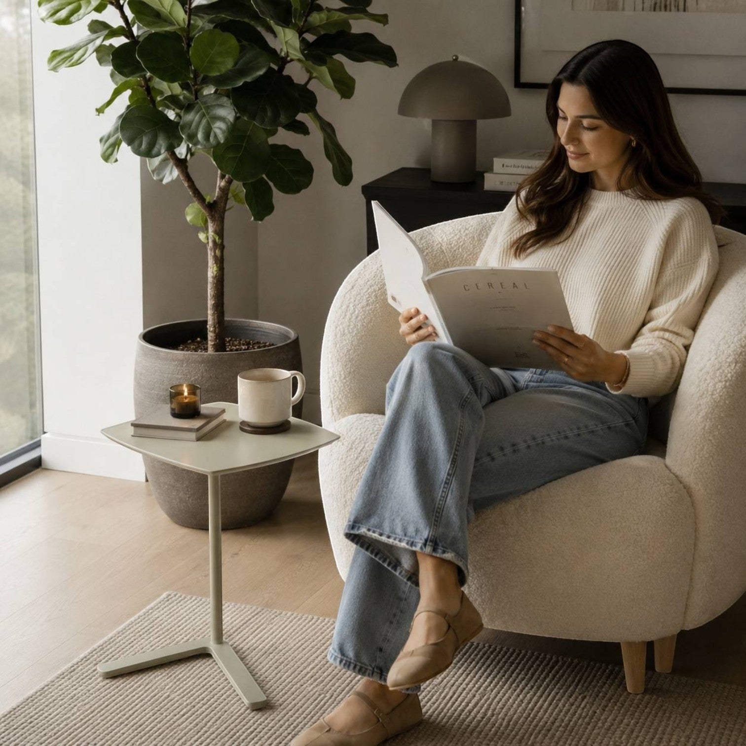 Addo Shop Dodo square side table with a minimalist cantilever base next to a woman reading in a white armchair.