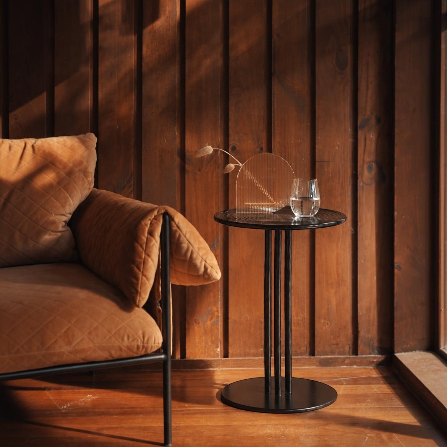 Addo Shop black metal side table with a glass of water and decorative arch piece next to a quilted brown armchair