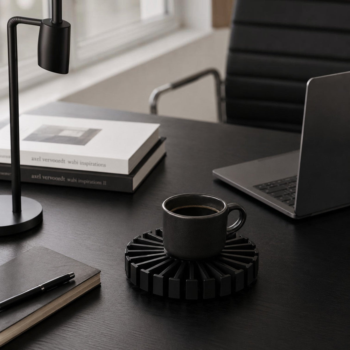 Addo Shop black circular ridged coaster holding a dark ceramic coffee mug on a minimalist office desk