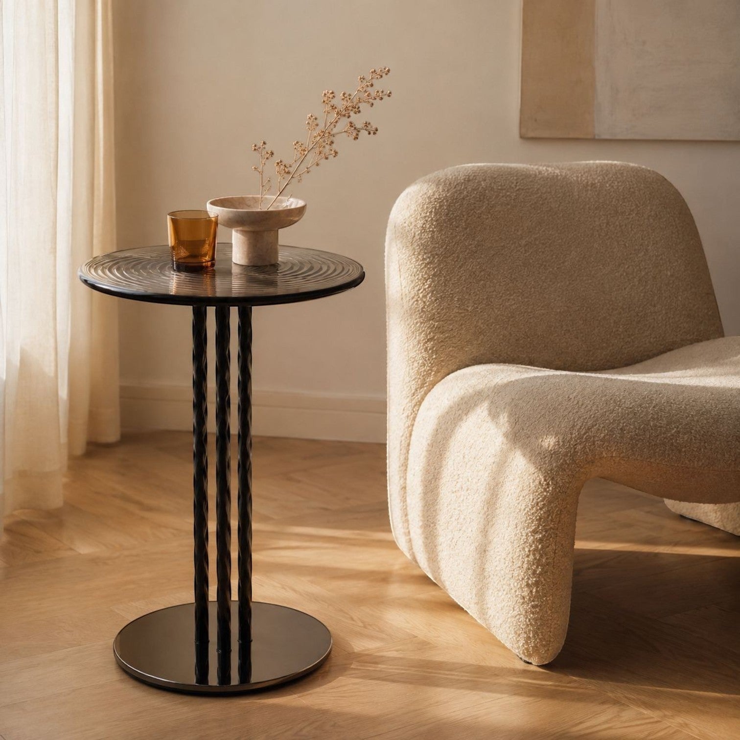 Addo Shop round black side table with spiral legs next to a beige textured boucle armchair in a sunlit room