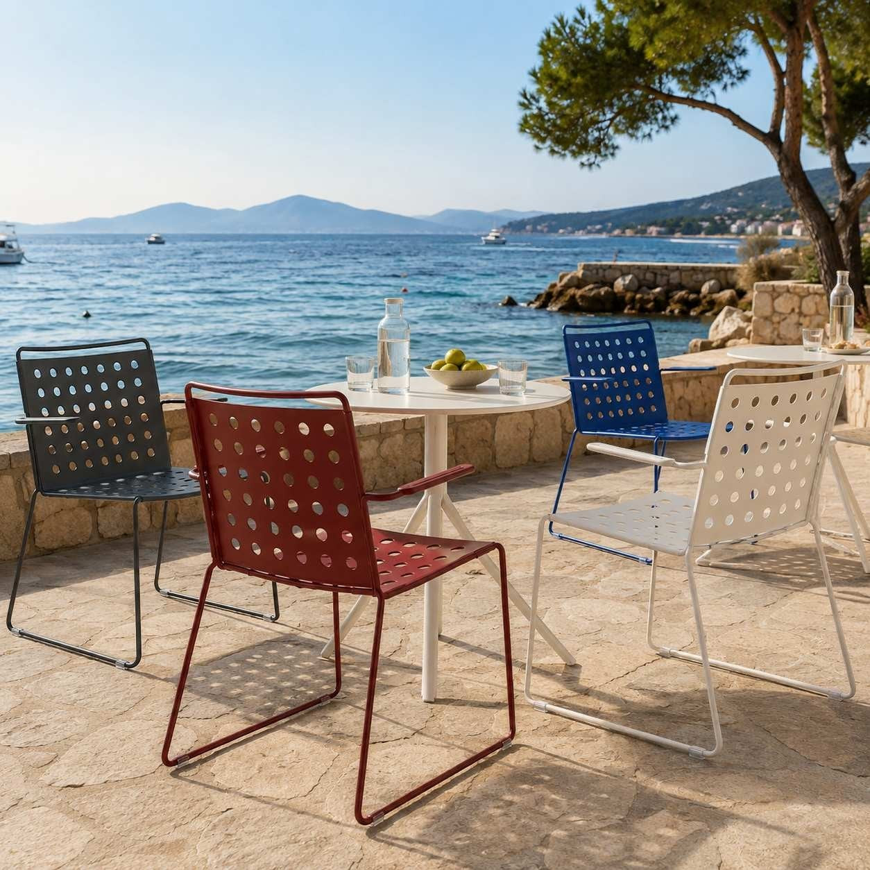 Addo Shop BUSY chairs with arms in red, white, blue, and black, featuring a perforated metal design on a patio.
