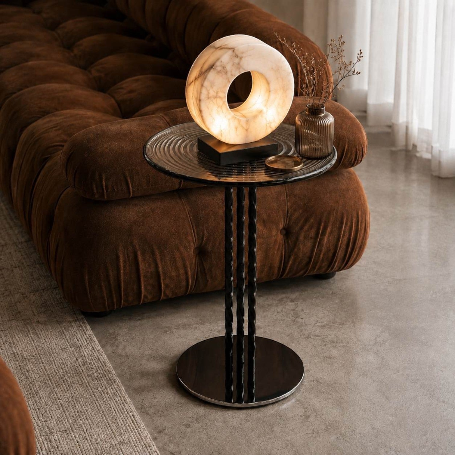 Addo Shop circular marble table lamp with a warm glow, set on a modern black metal side table in a cozy living room.