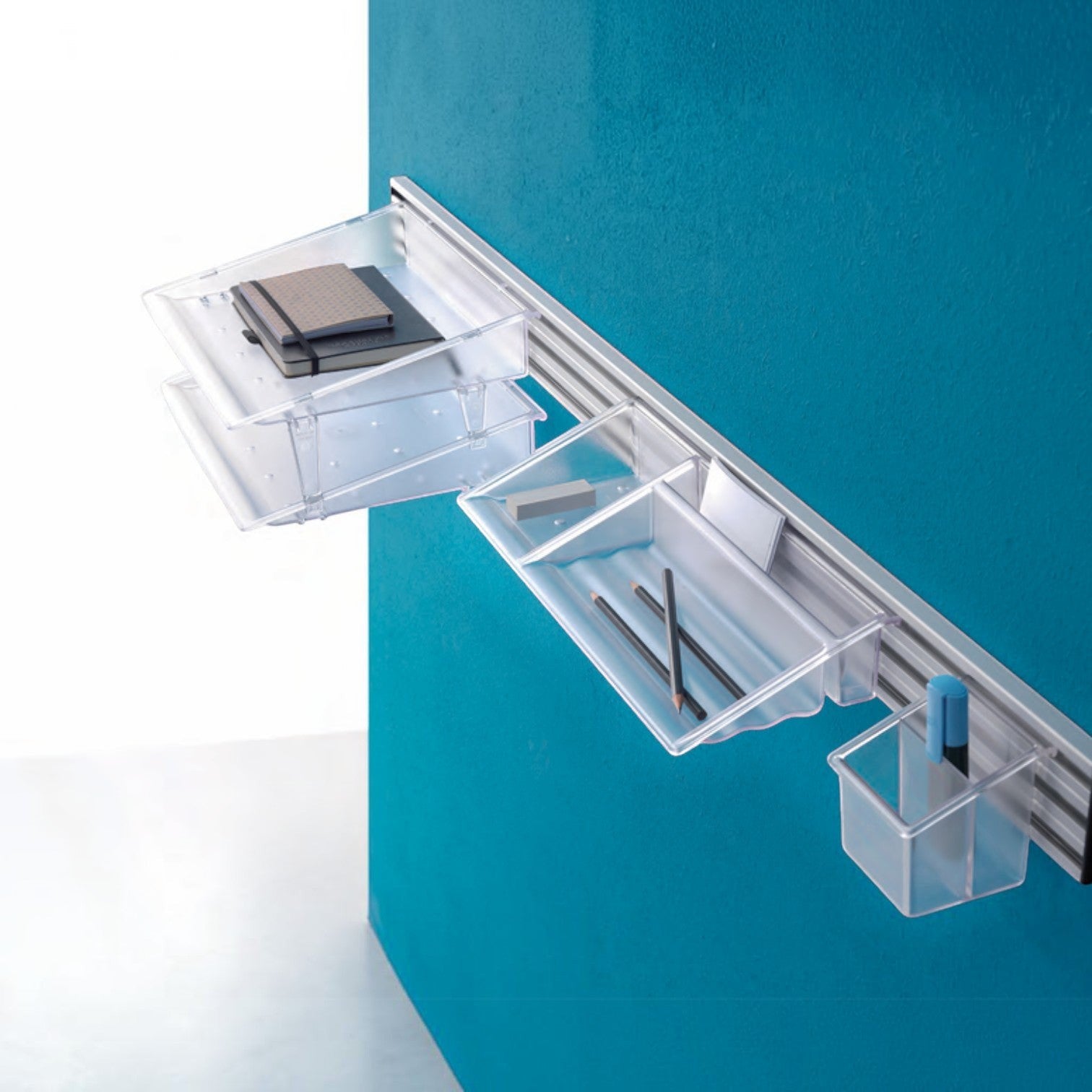 Addo Shop Desk-Up clear plastic wall-mounted organizer system with trays and pencil holder on a blue wall.