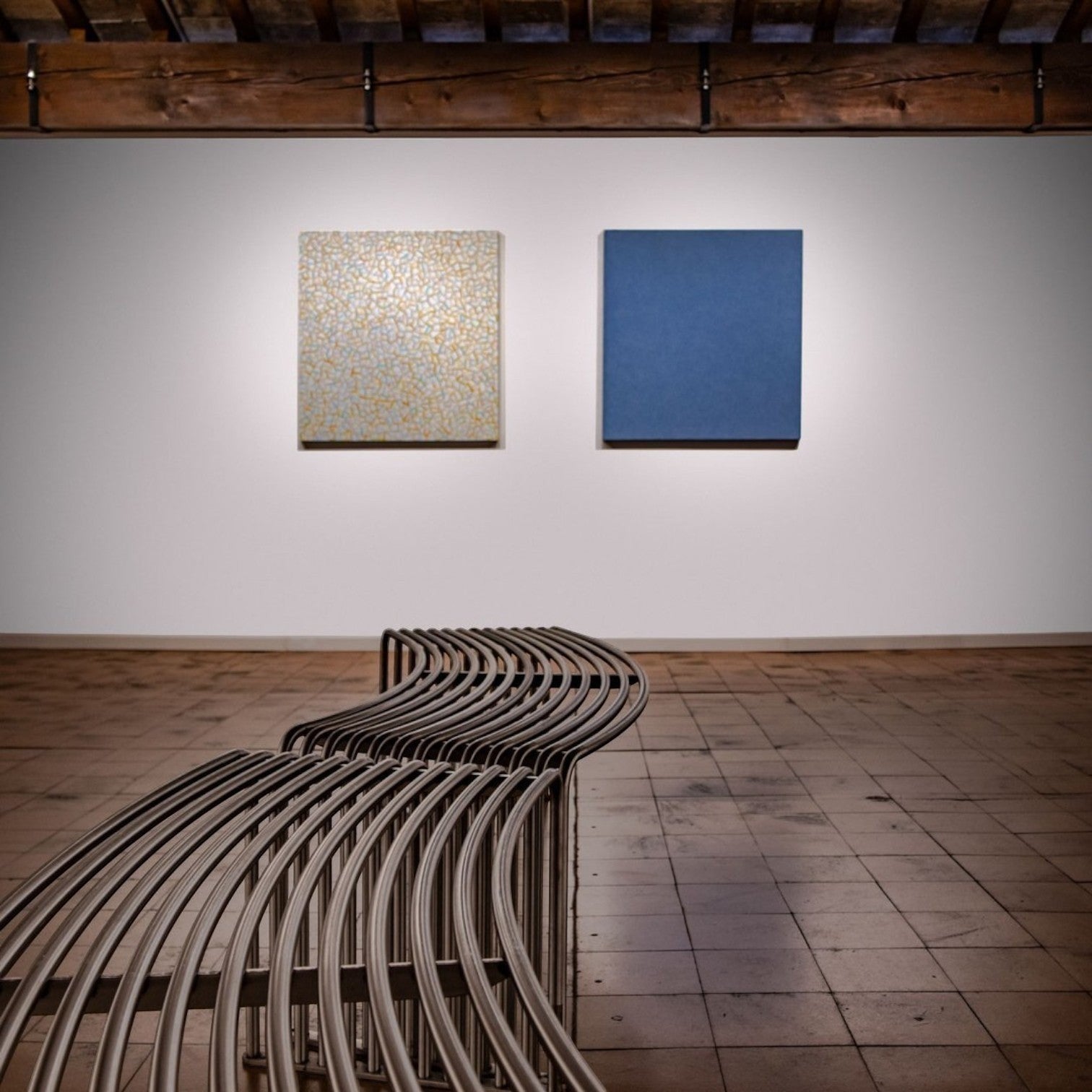 Addo Shop DIEMMEBI .015 curved steel bench in a gallery setting with modern art on the wall.