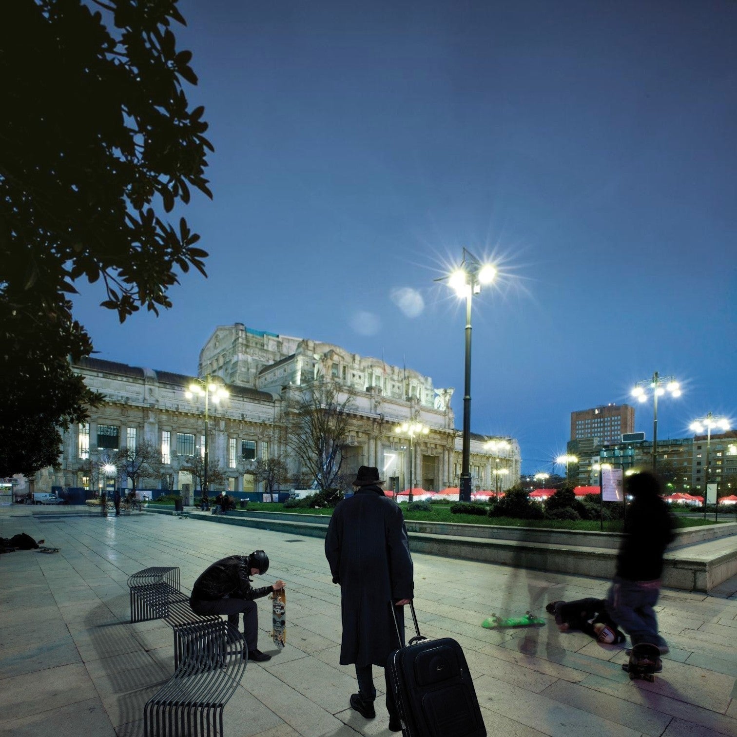 Addo Shop DIEMMEBI .015 concave outdoor steel bench in a public city square with skaters and commuters at dusk.