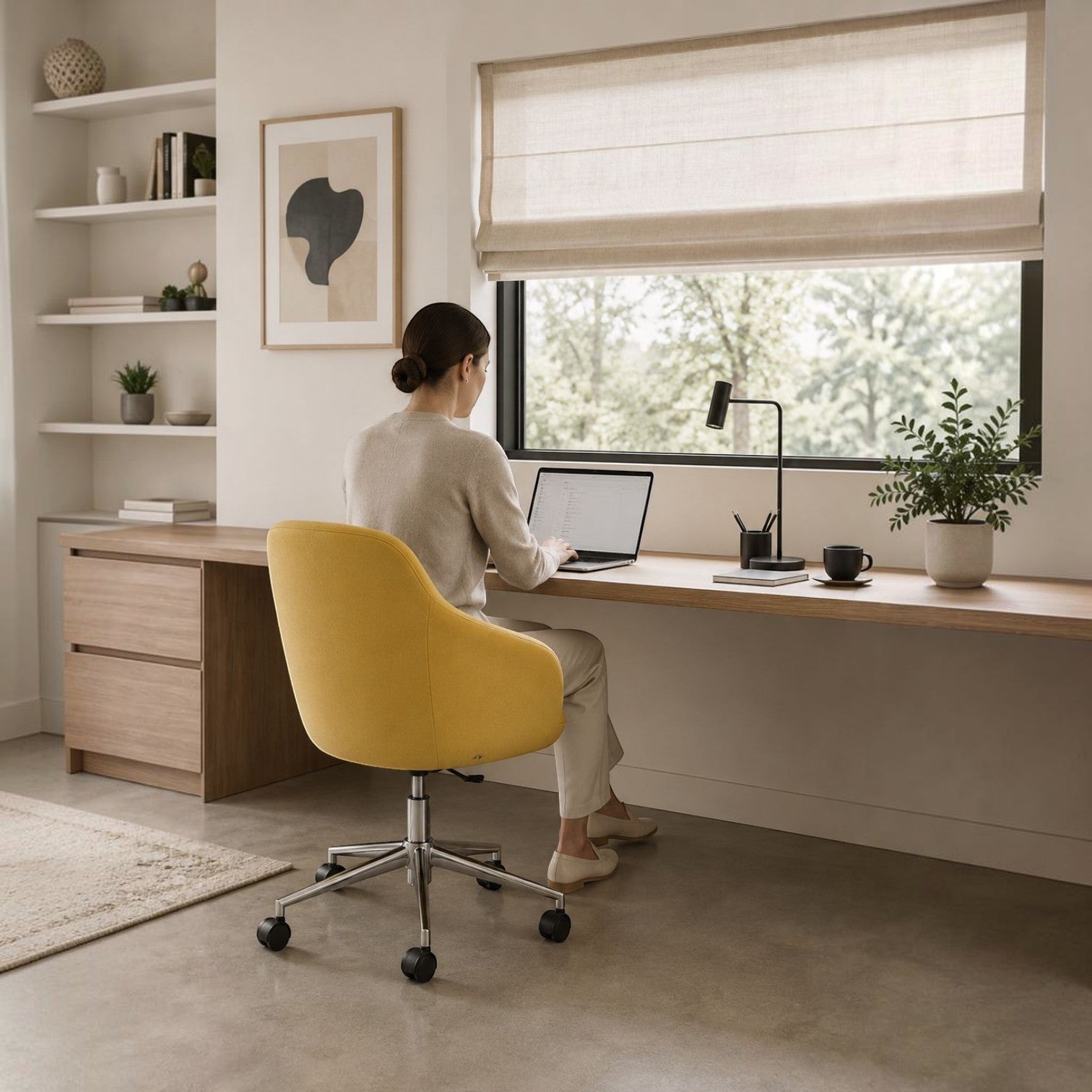 Woman working on a laptop in a bright home office sitting on a yellow Addo Shop Gio office chair with chrome base.