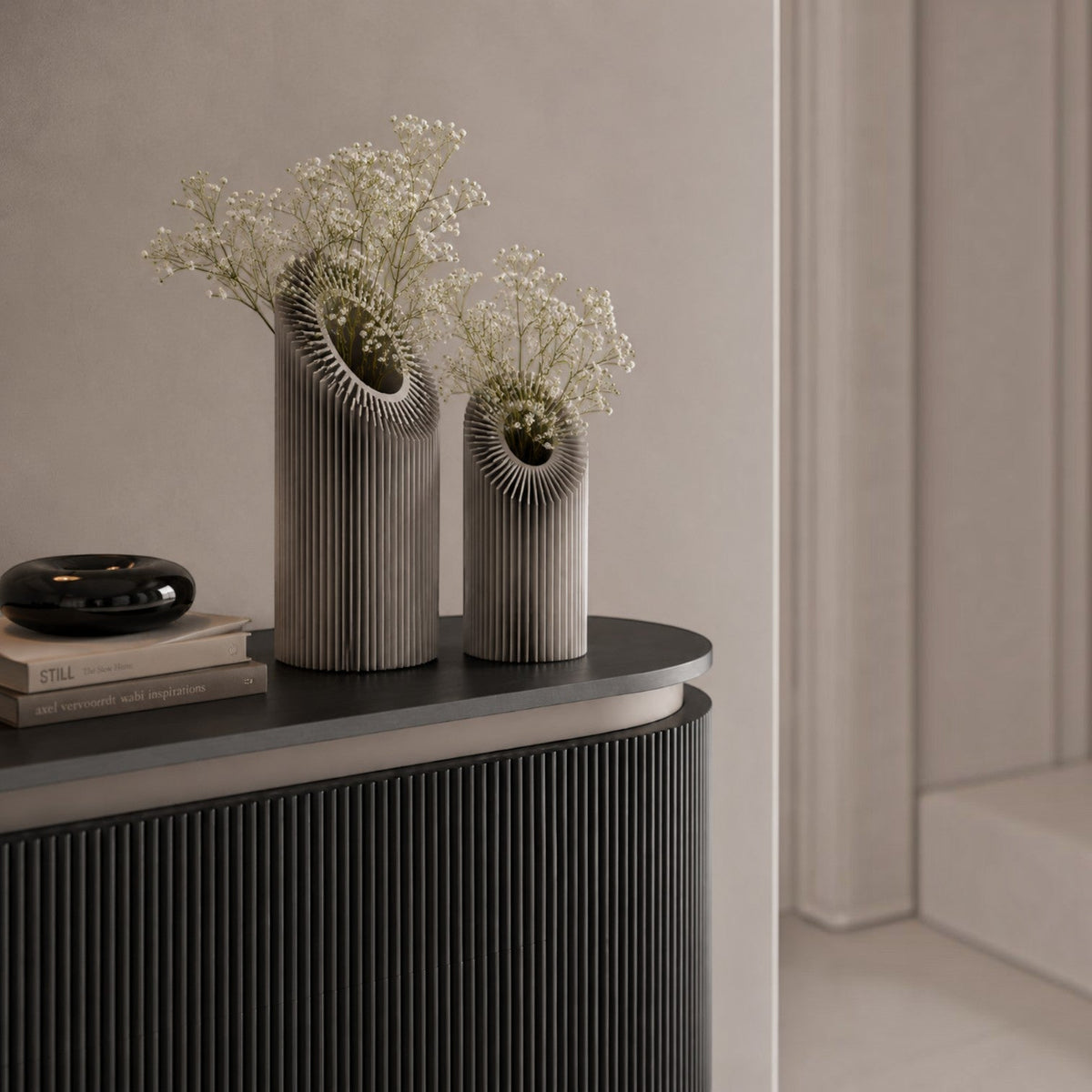 Addo Shop Helio sculptural metal decorative objects with ribbed cylindrical bodies and white flowers on a console.