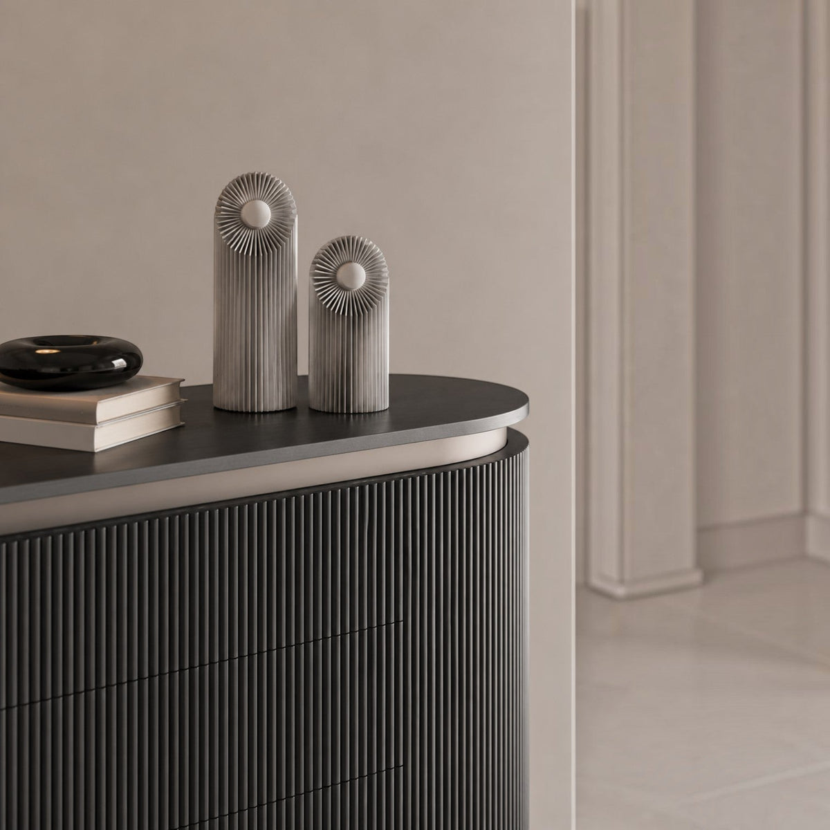 Addo Shop Helio metal decorative objects with ribbed cylindrical bodies and circular tops on a dark console table.
