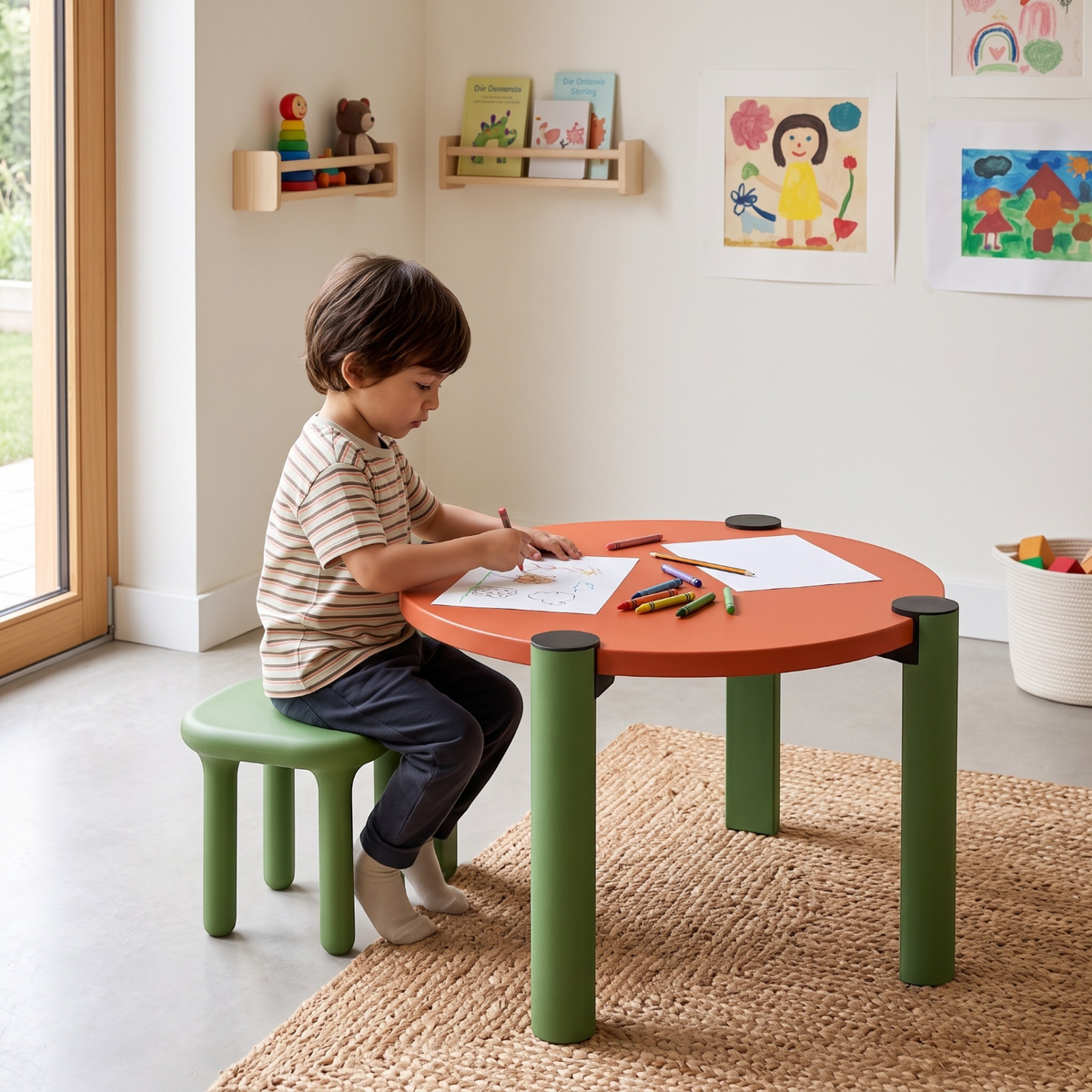A young boy drawing at an Addo Shop Kidzdesk01 round orange table with green legs and a matching green stool.