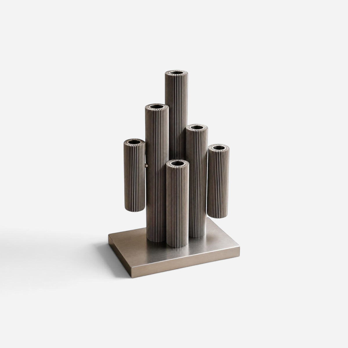 Addo Shop MUMMY sculptural candle holder made of brushed aluminum with cylindrical ribbed forms on a rectangular base.