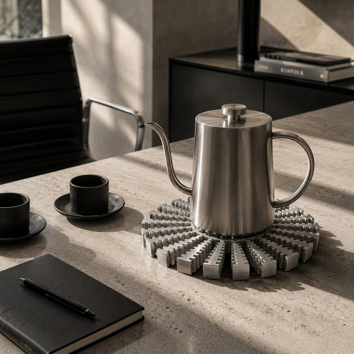Addo Shop NE-HALE brushed aluminum radial trivet holding a stainless steel kettle on a stone kitchen countertop