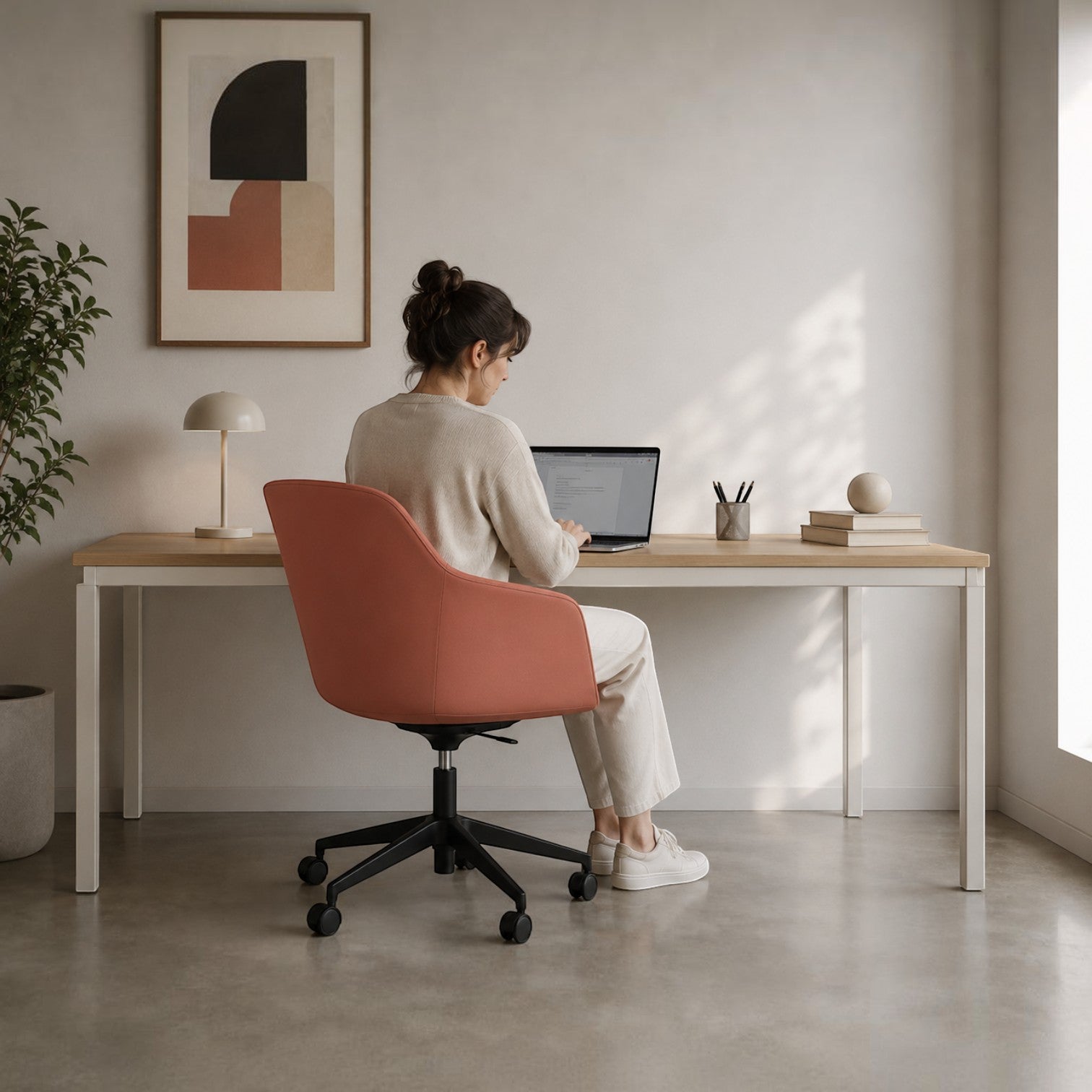 Woman sitting on a coral Addo Shop Payal office chair with a 4-star swivel base at a wooden desk in a modern room.
