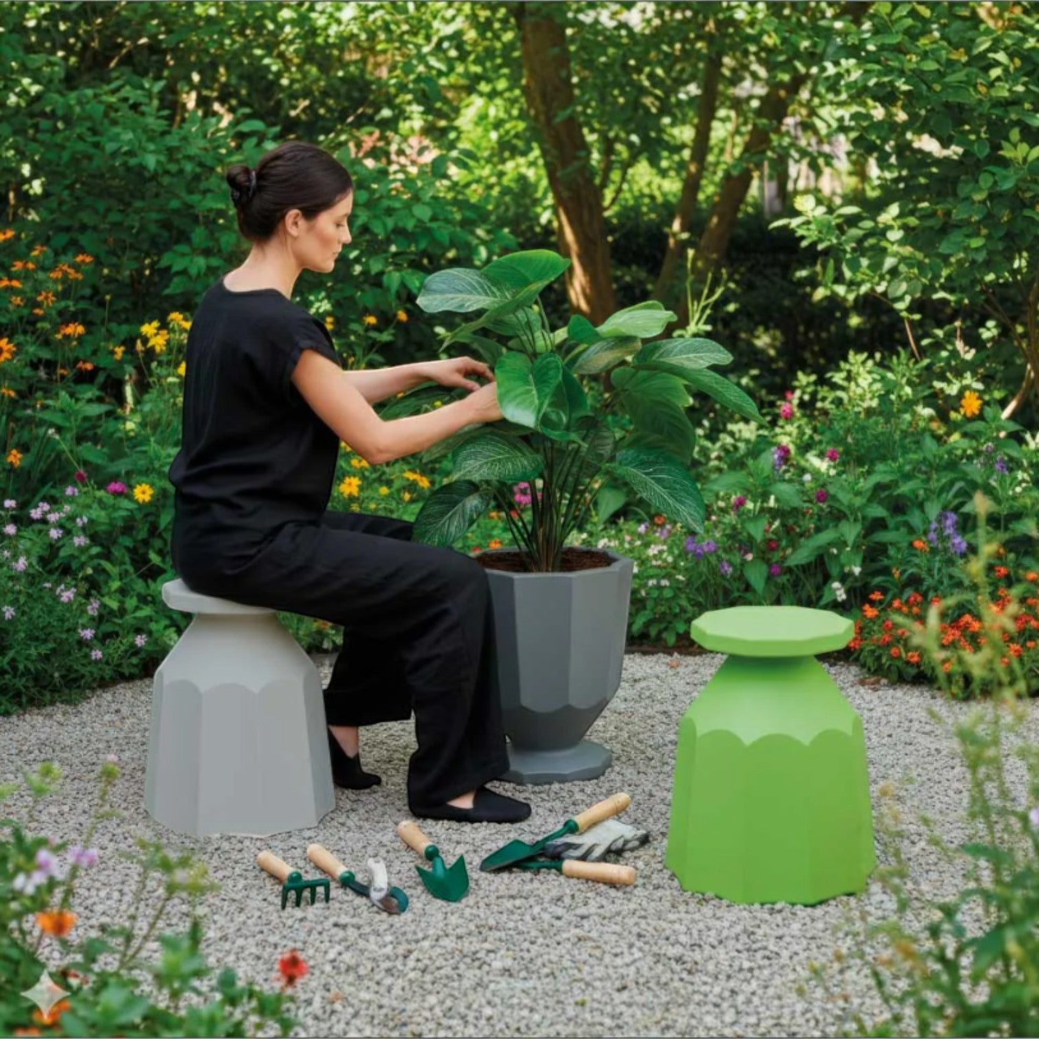 Woman in black sitting on a grey Addo Shop Rerecycled Stool in a garden next to a bright green stool and plants.