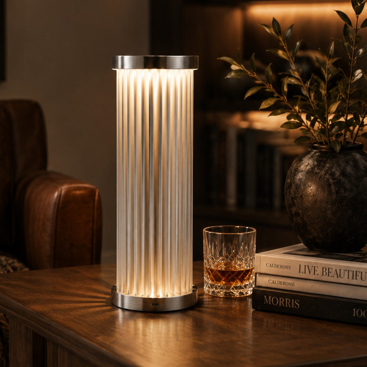 Addo Shop cylindrical table lamp with ribbed glass shade and brushed metal base emitting a warm glow on a desk