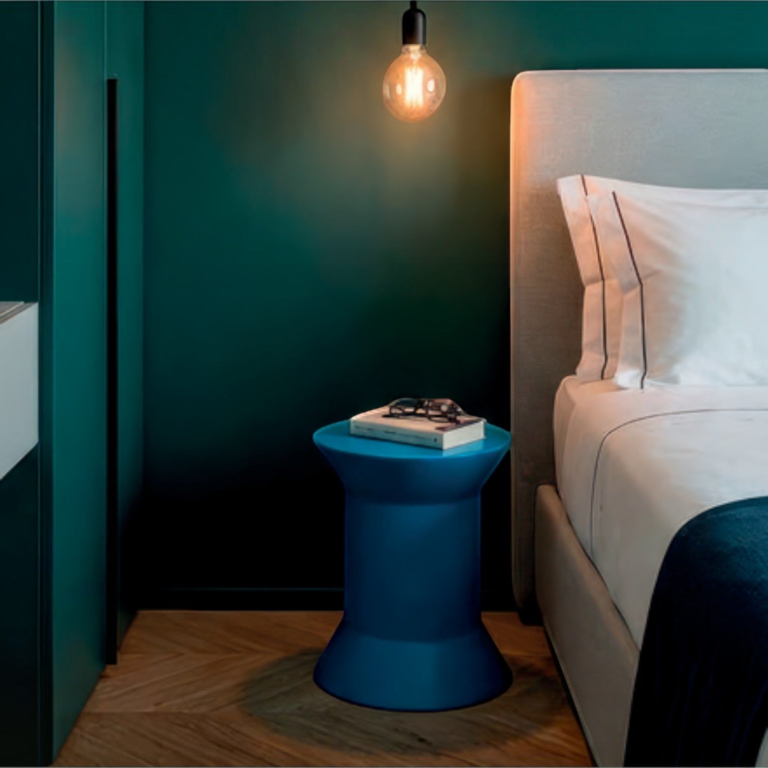 Addo Shop STILEMI Round blue side table with a modern spool-shaped design in a contemporary bedroom setting.
