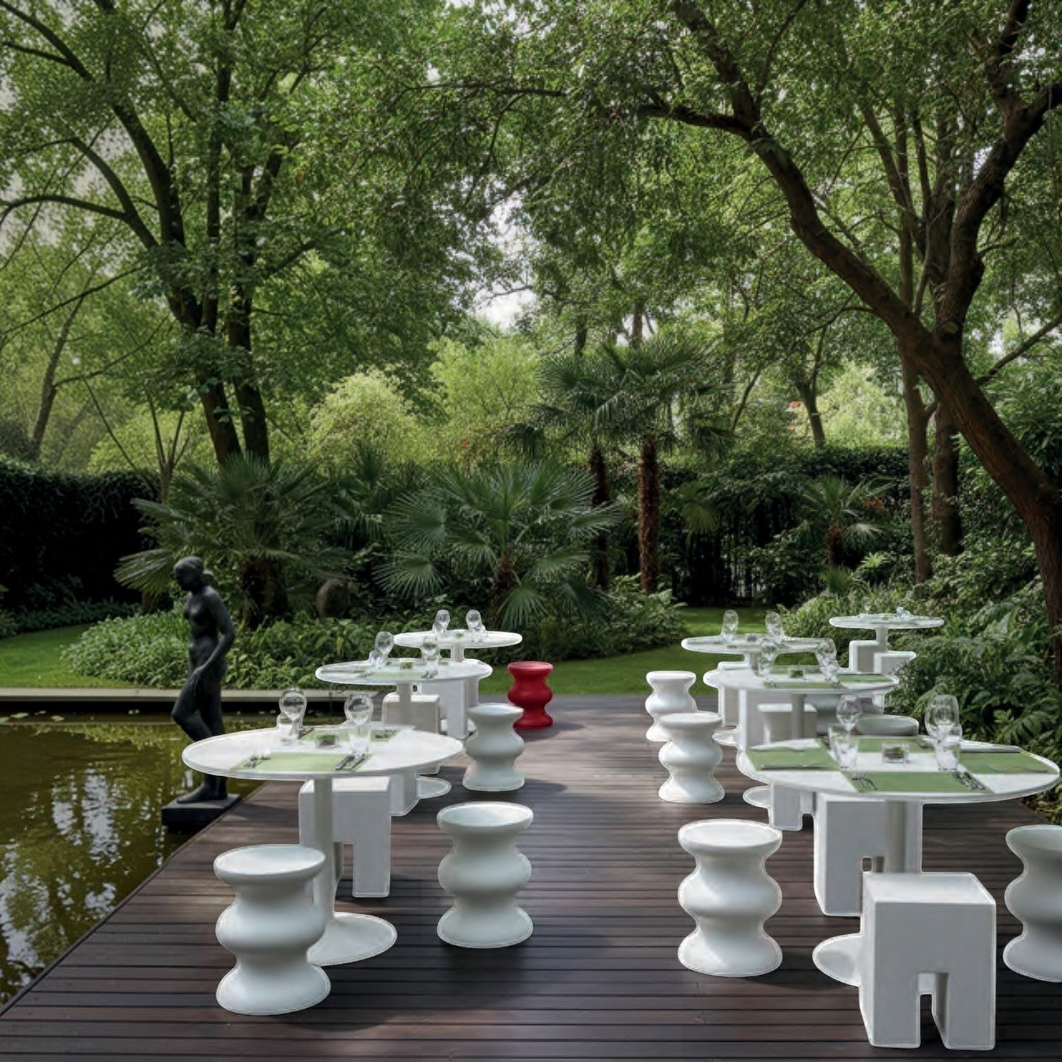Addo Shop STILEMI Sculptural white stools and round tables arranged on a wooden deck in a lush garden setting.
