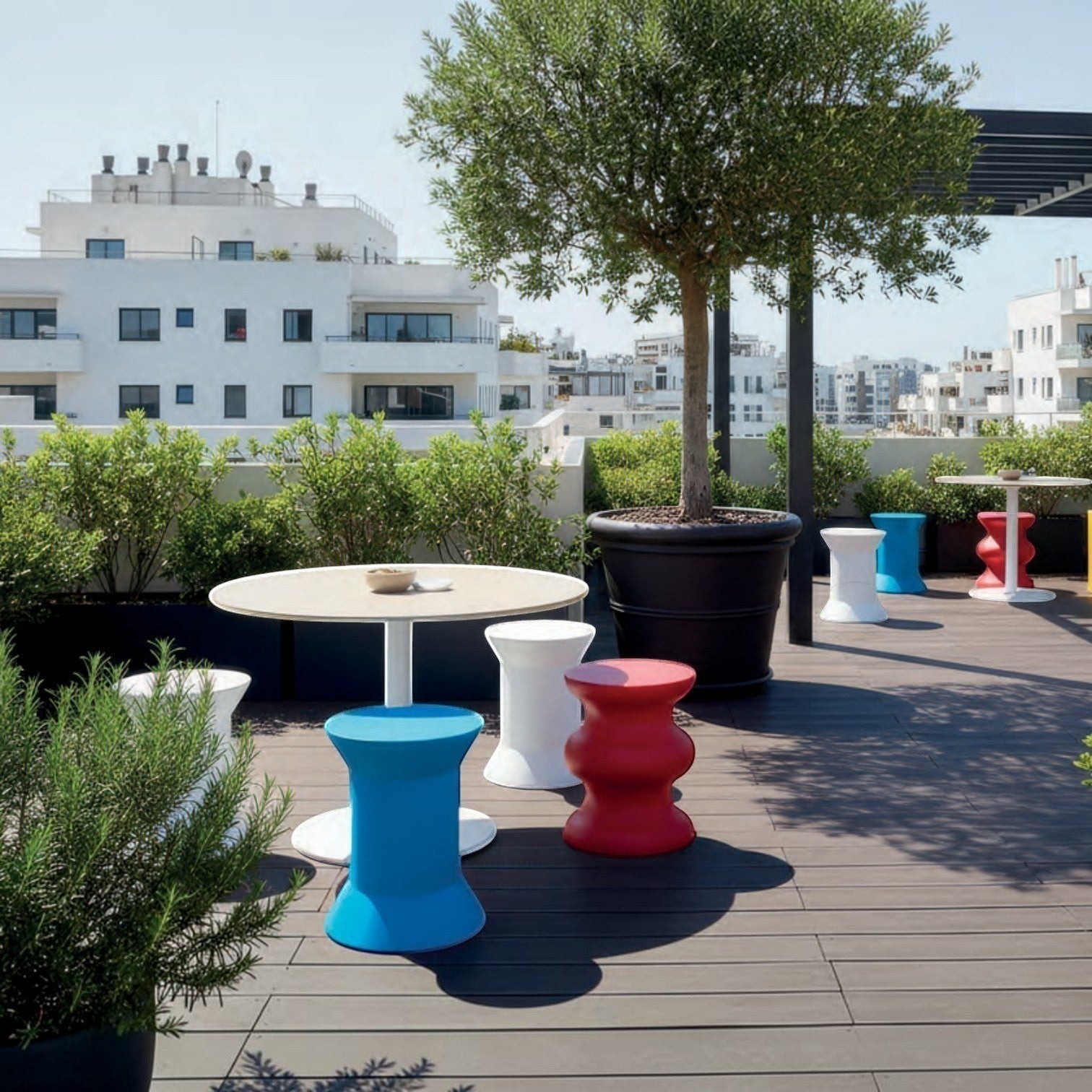 Addo Shop STILEMI Sculptural stools in red, white, and blue on a modern outdoor rooftop terrace with round tables.