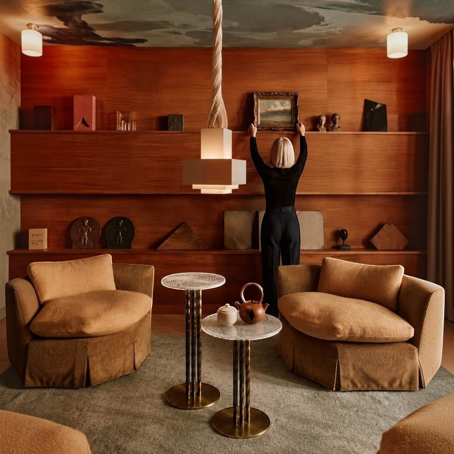 Addo Shop interior design featuring two tan armchairs, marble side tables, and a woman arranging art on wood shelves.