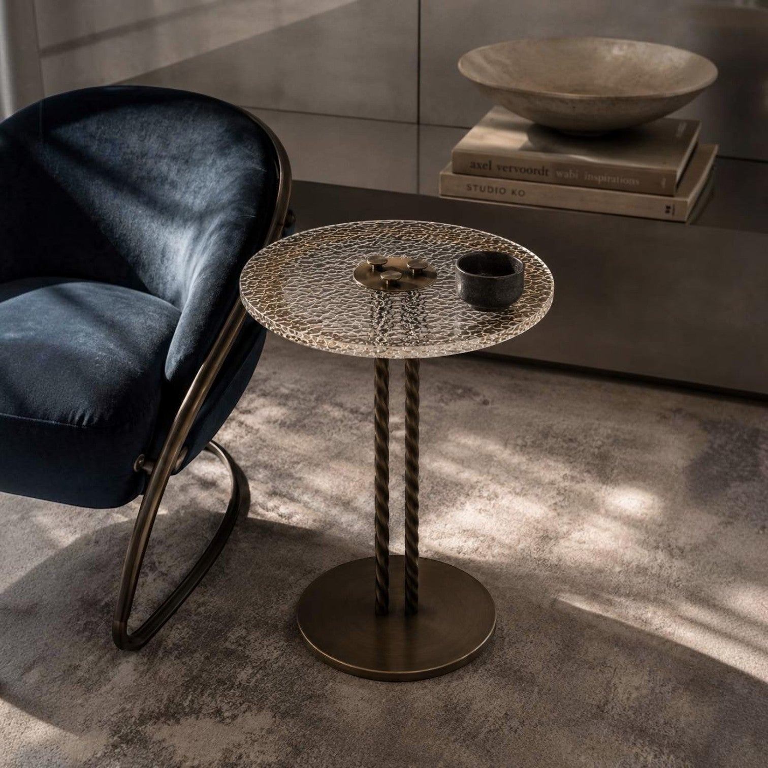Addo Shop round side table with a textured glass top and twisted bronze metal base in a modern living room setting