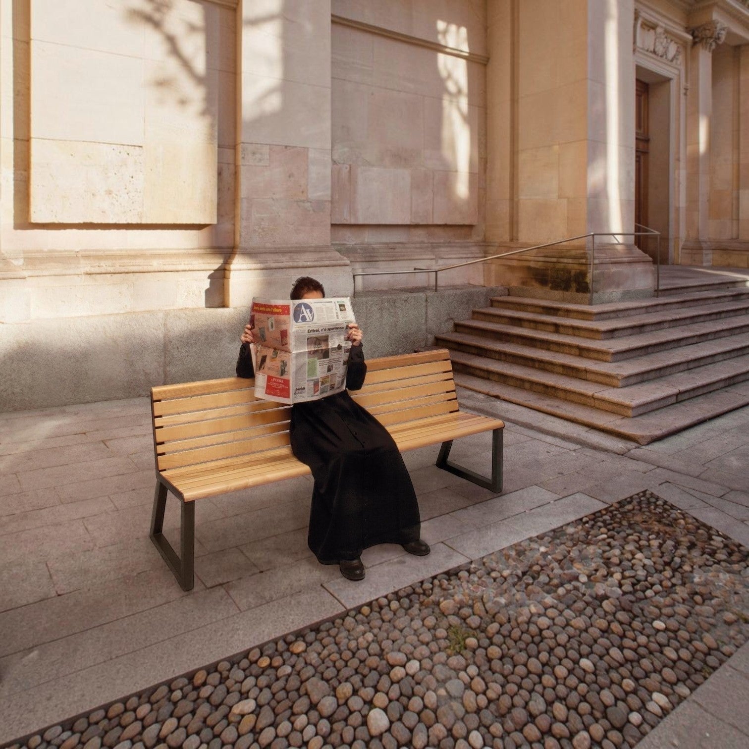 Addo Shop Ventiquattrore.h24 wooden bench with backrest and dark metal frame, occupied by a person reading a newspaper.