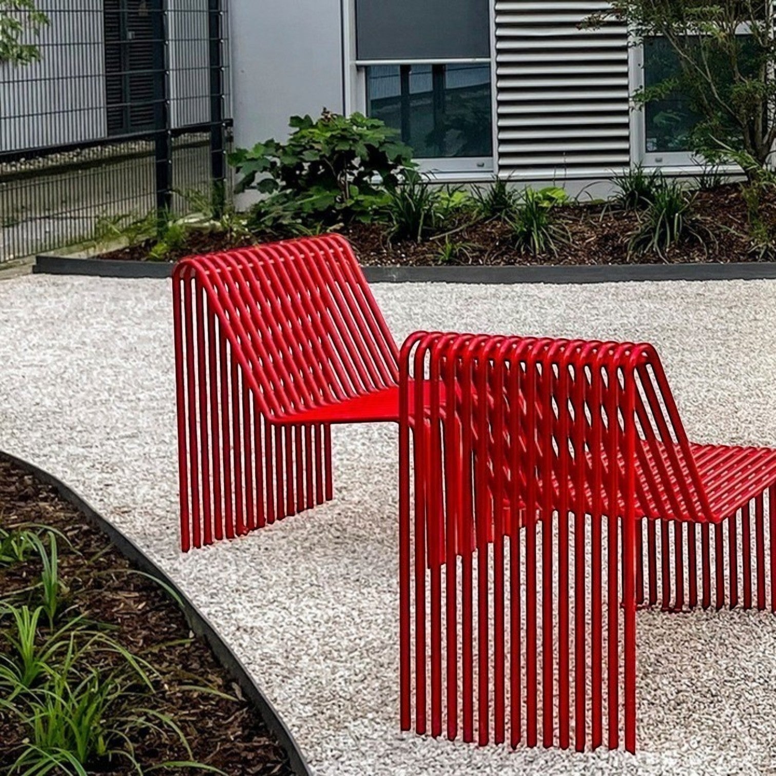 Addo Shop Zeroquindici .015 red metal slatted outdoor seat modules arranged on a gravel garden path.