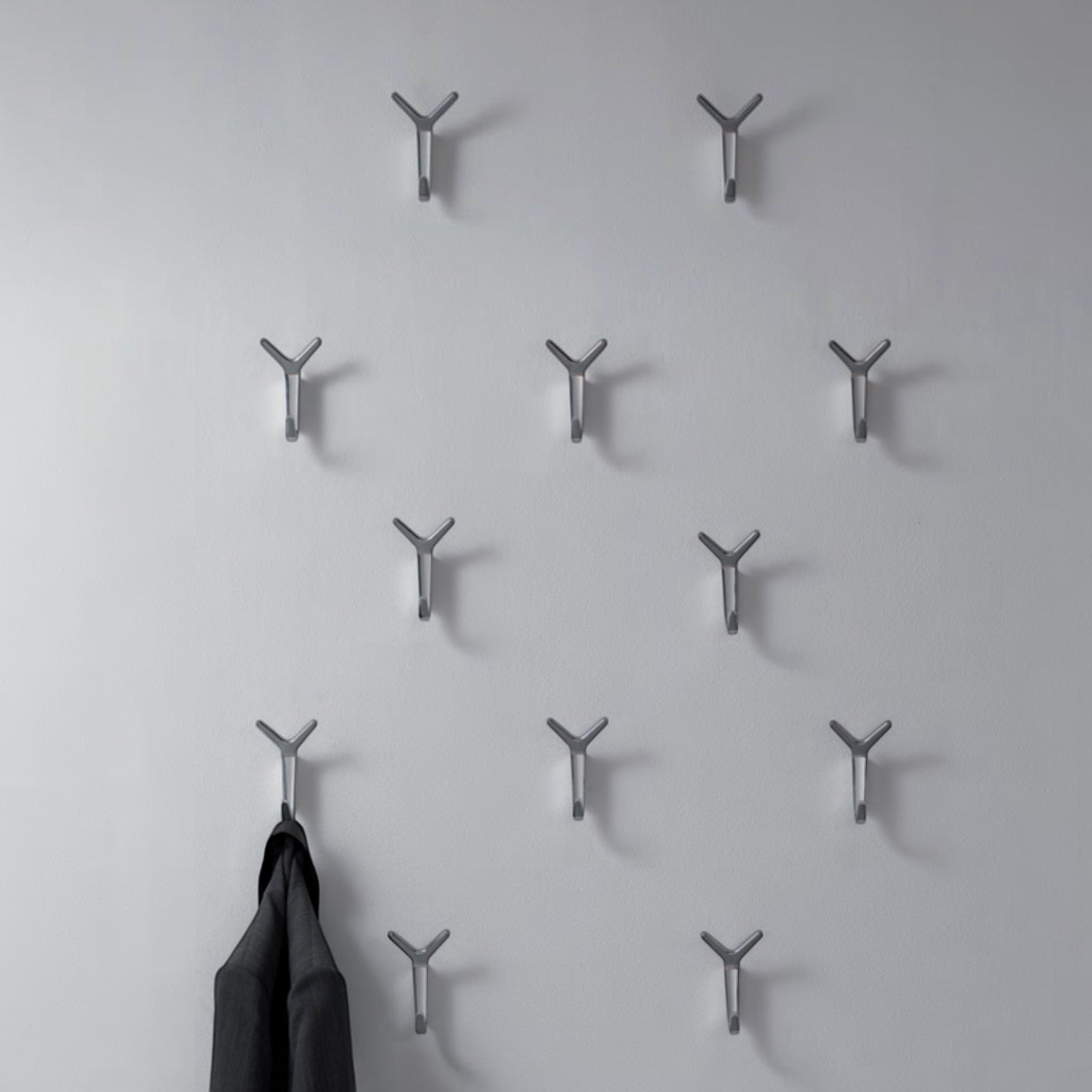 Addo Shop Battista hook coat rack with 12 silver metal Y-shaped hooks mounted on a white wall. One hook holds a dark jacket.