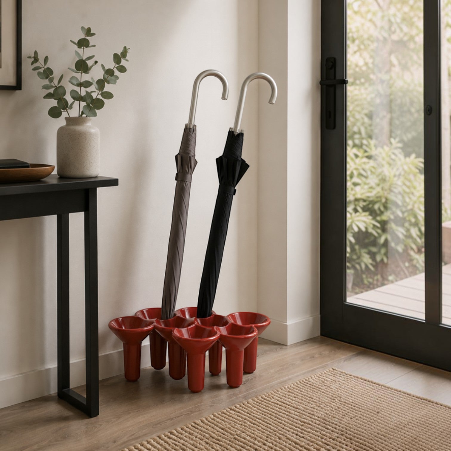 Addo Shop KABO umbrella stand in red, holding two umbrellas in grey and black.