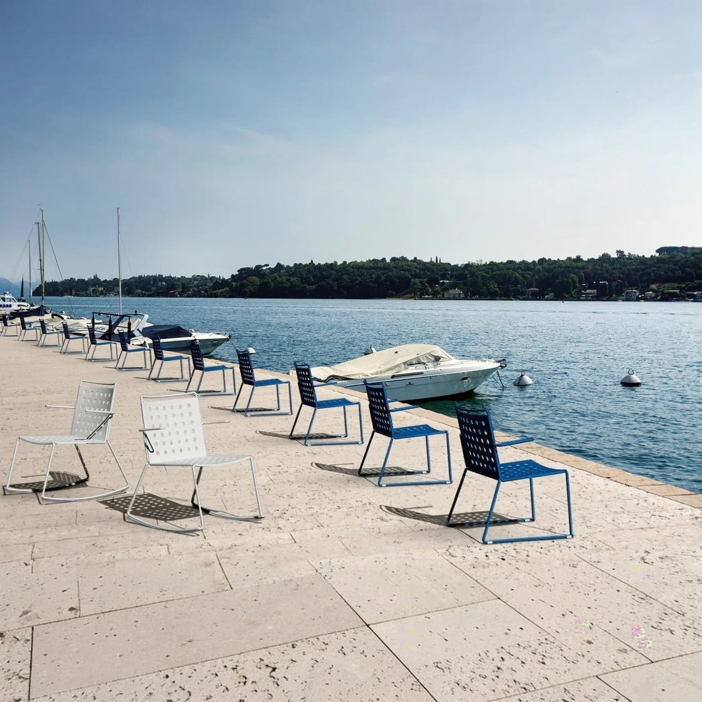 Addo Shop white and blue powder-coated steel outdoor chairs with perforated seats, arranged on a stone patio by the water.