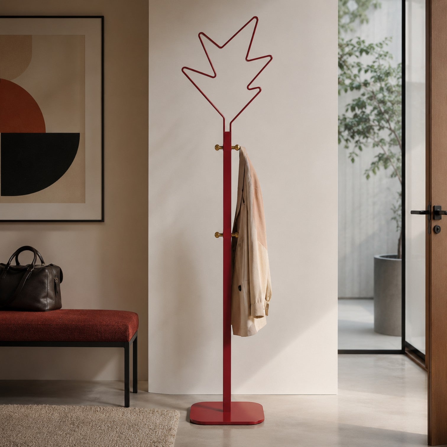 Addo Shop Stella red metal coat stand with leaf-shaped top and brass hooks, holding a beige trench coat.