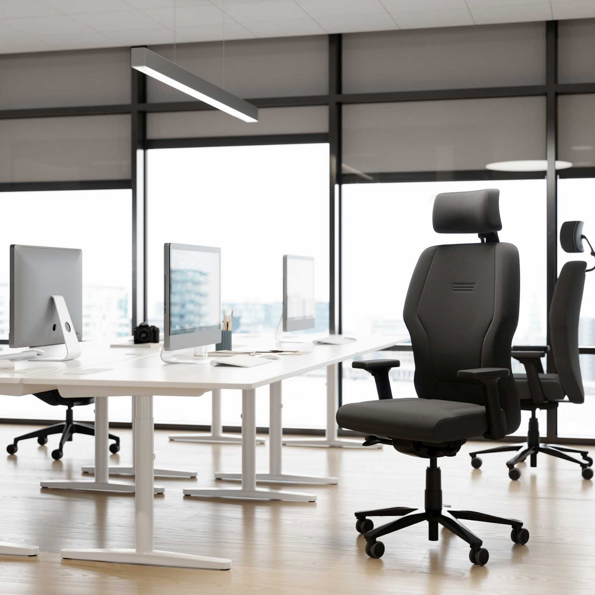 Interstuhl XXL çalışma koltuğu açık ofis ortamında, koyu gri kumaş döşeme ve başlık, beyaz masaların yanında